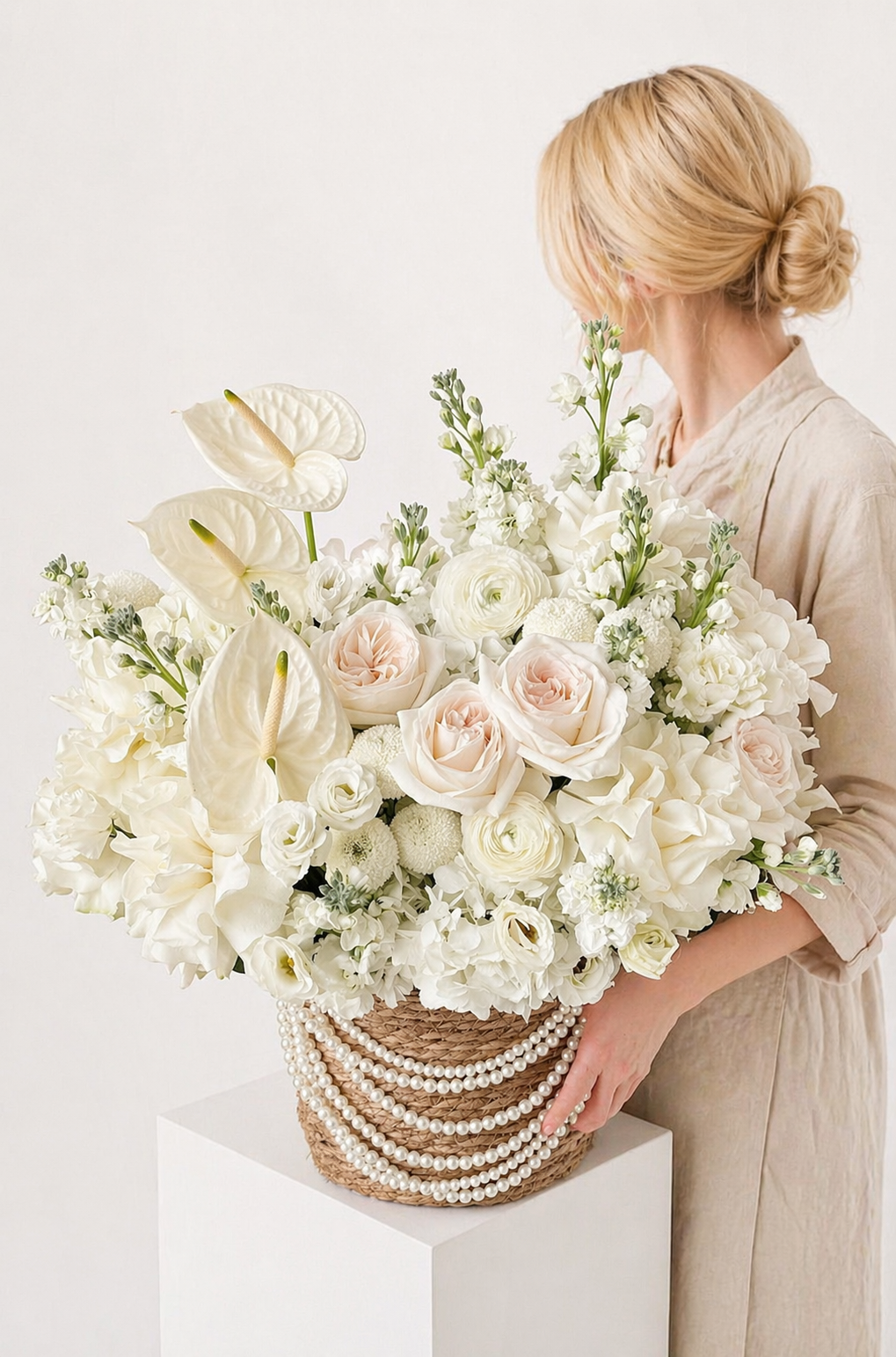 Fresh ivory flower arrangement in a basket with pearl accents held by woman in beige dress